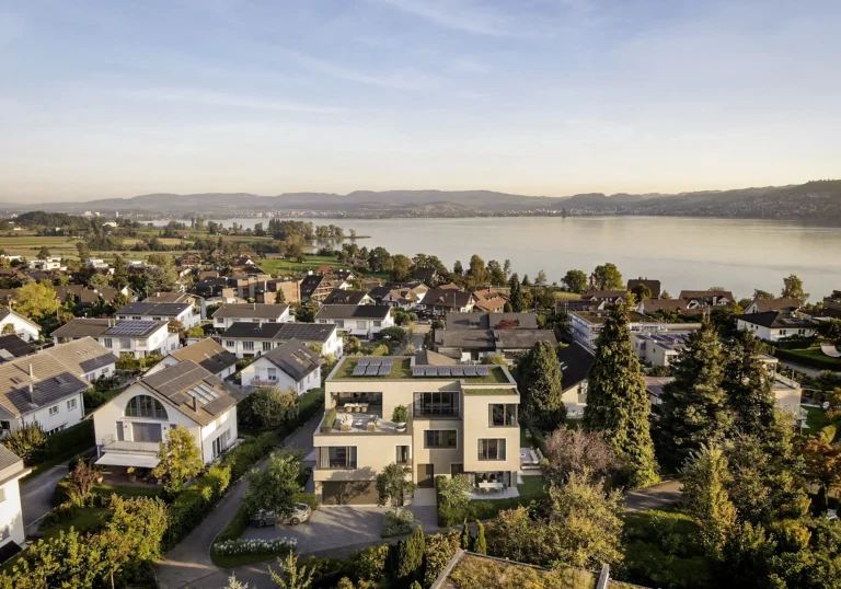 Vogelperspektive des Zweifamilienhauses N7 in Buonas mit begrüntem Flachdach, Solaranlage und Zugersee im Hintergrund.