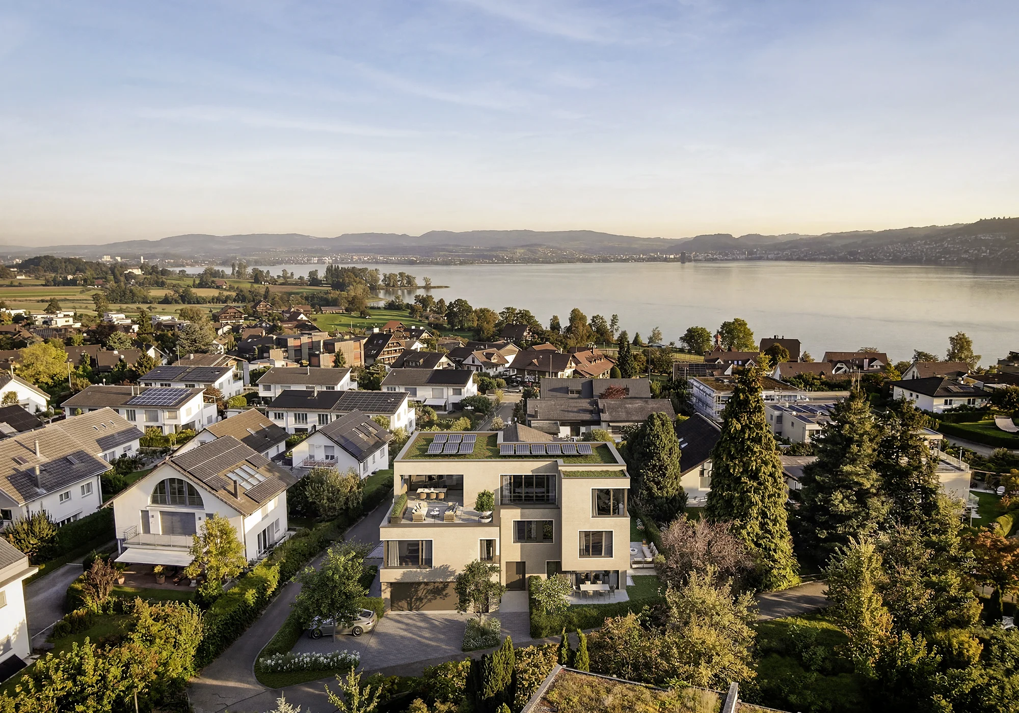 Vogelperspektive des Zweifamilienhauses N7 in Buonas mit begrüntem Flachdach, Solaranlage und Zugersee im Hintergrund.